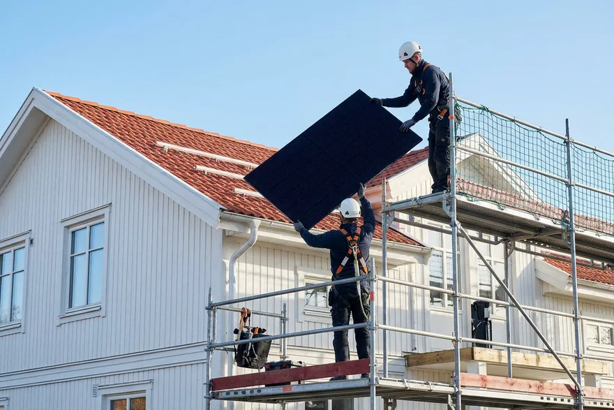 Montörer lyfter solpaneler på plats på ett villatak